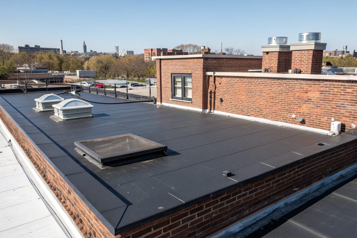 A new black rubber flat roof with skylights on a brick building, with a city skyline behind