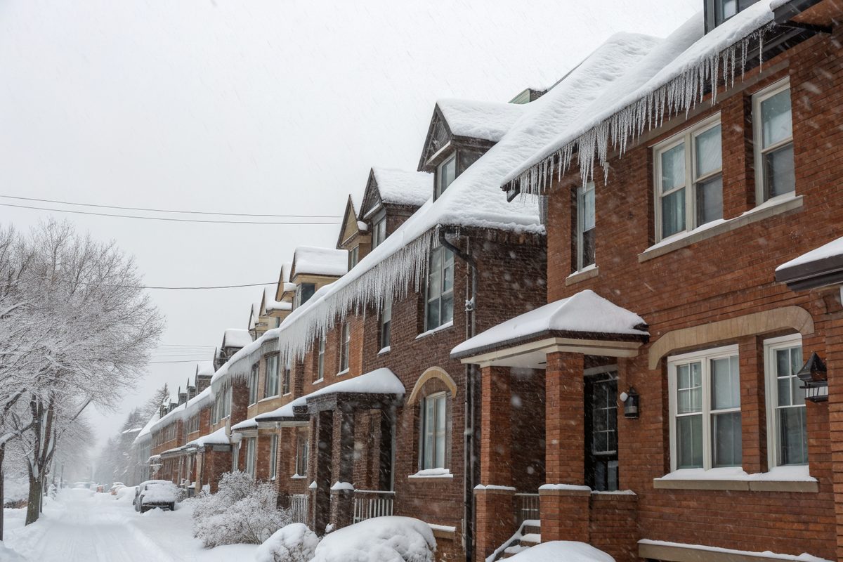 Snow and icicles on the roofs of a row of brick houses on a quiet winter street